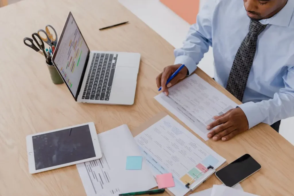 High-angle shot of a businessman in a tie reviewing documents at a clean desk with a laptop and tablet